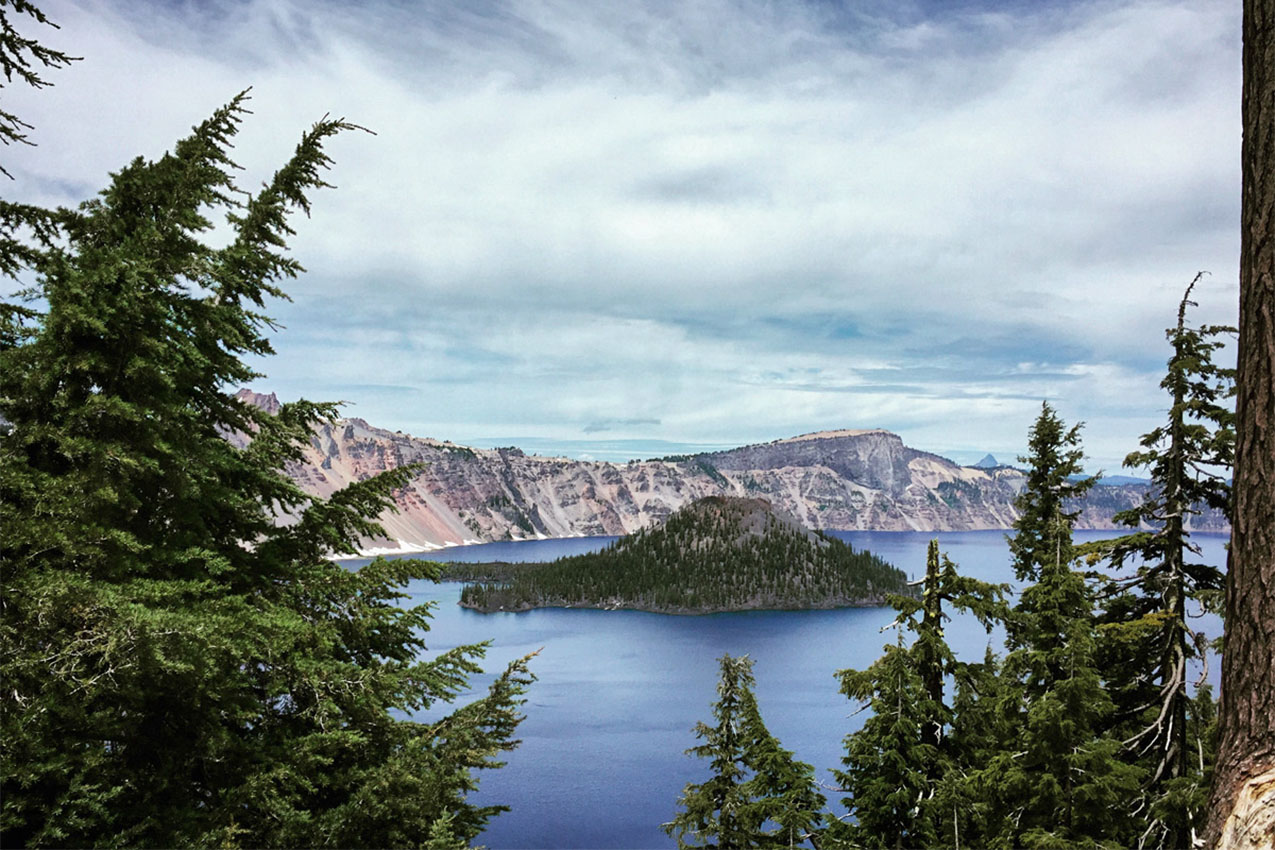 Tree covered island in the middle of a blue lake with a mountain range in the background.