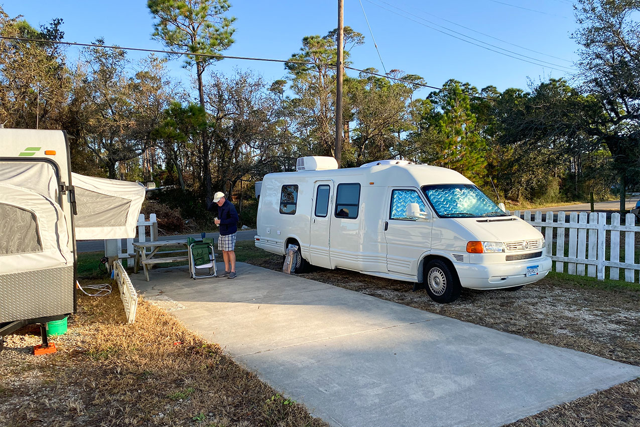 A man standing between a pop-up camper and a class B at an RV park.