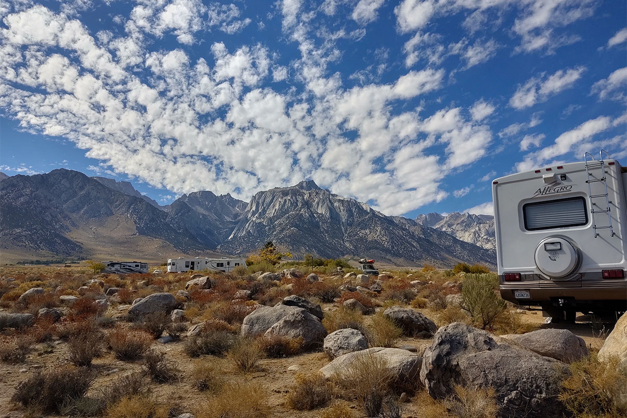 Several RVs parked in a field of boulders and shrubs at the base of large mountains.