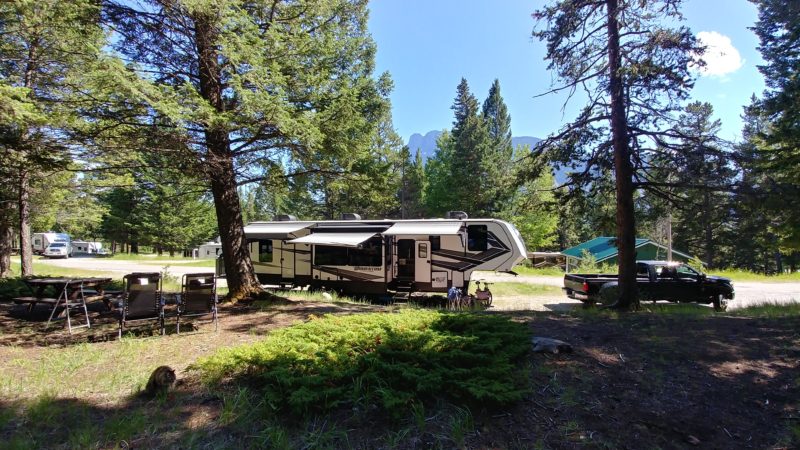 Large trailer parked at wooded campsite with mountain views