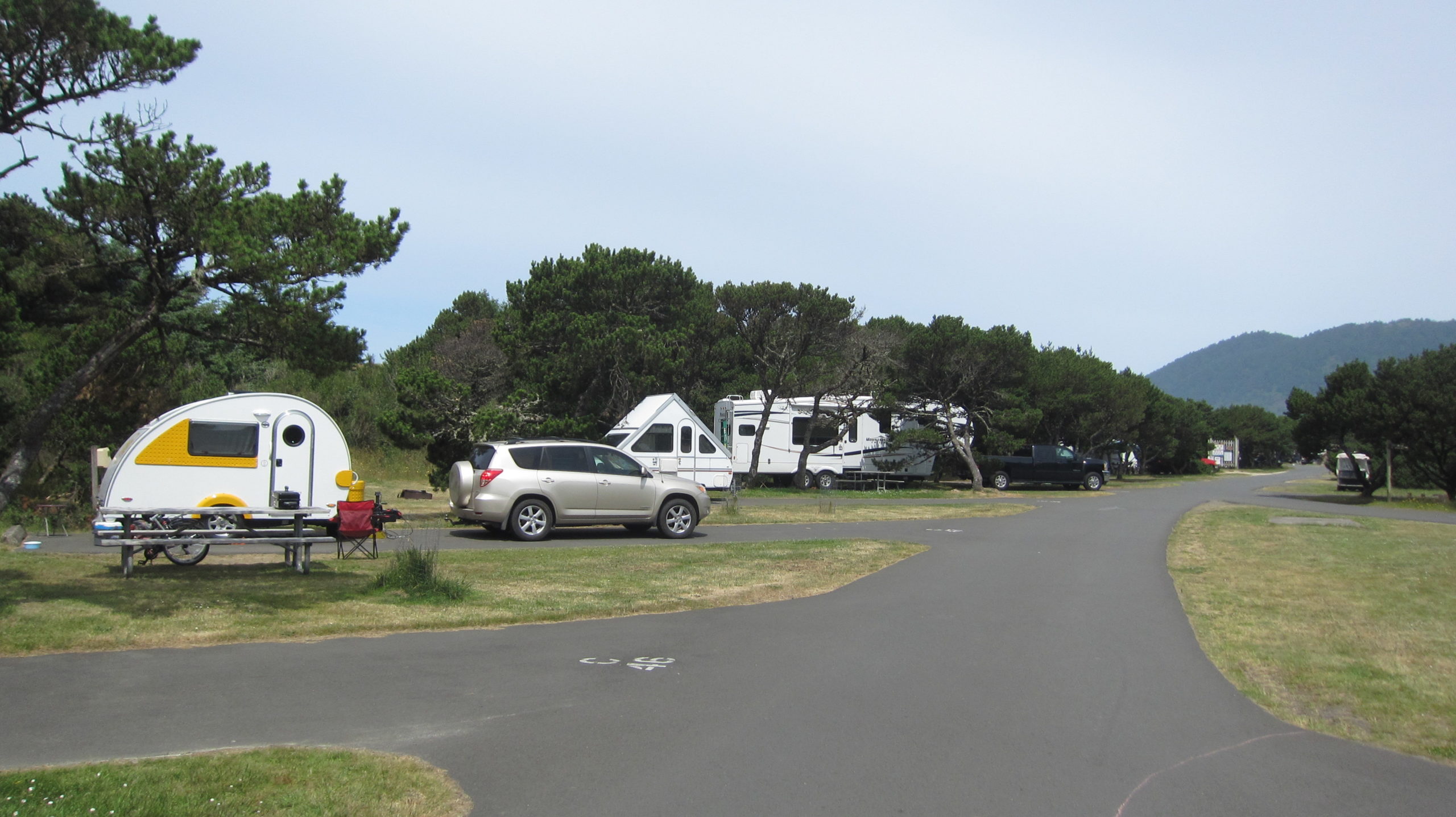 An SUV parked in front of a teardrop trailer at a campsite
