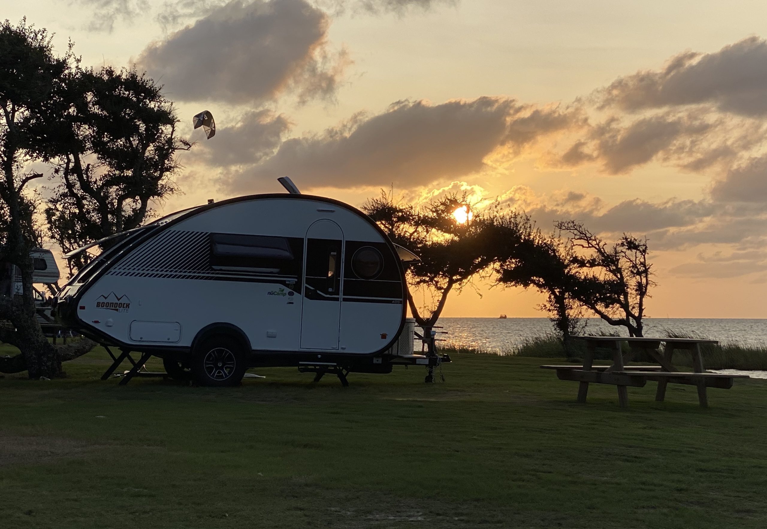 Teardrop travel trailer parked at a campsite with water in the background.