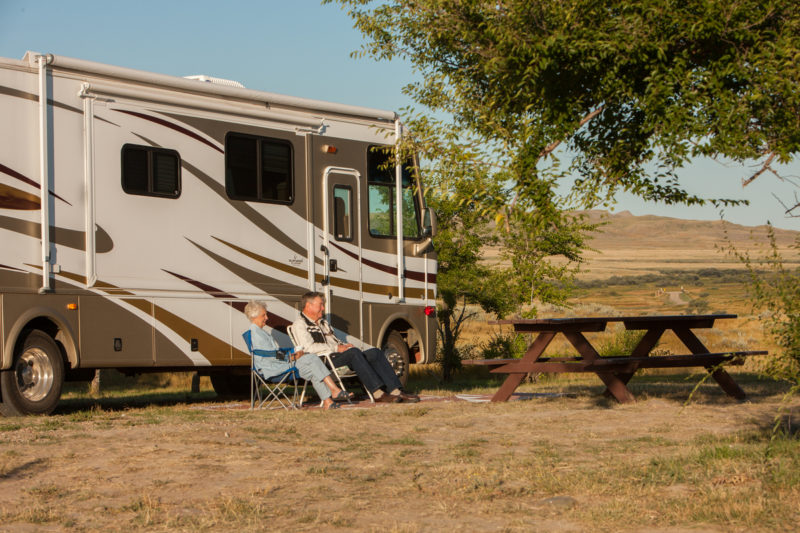 A man and a women sit on a chair near their vehicle look at the landscape