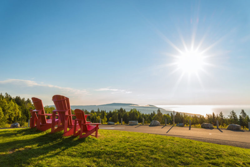 A row of red chairs on a grassy hill overlooking a shoreline as the sun is about to set