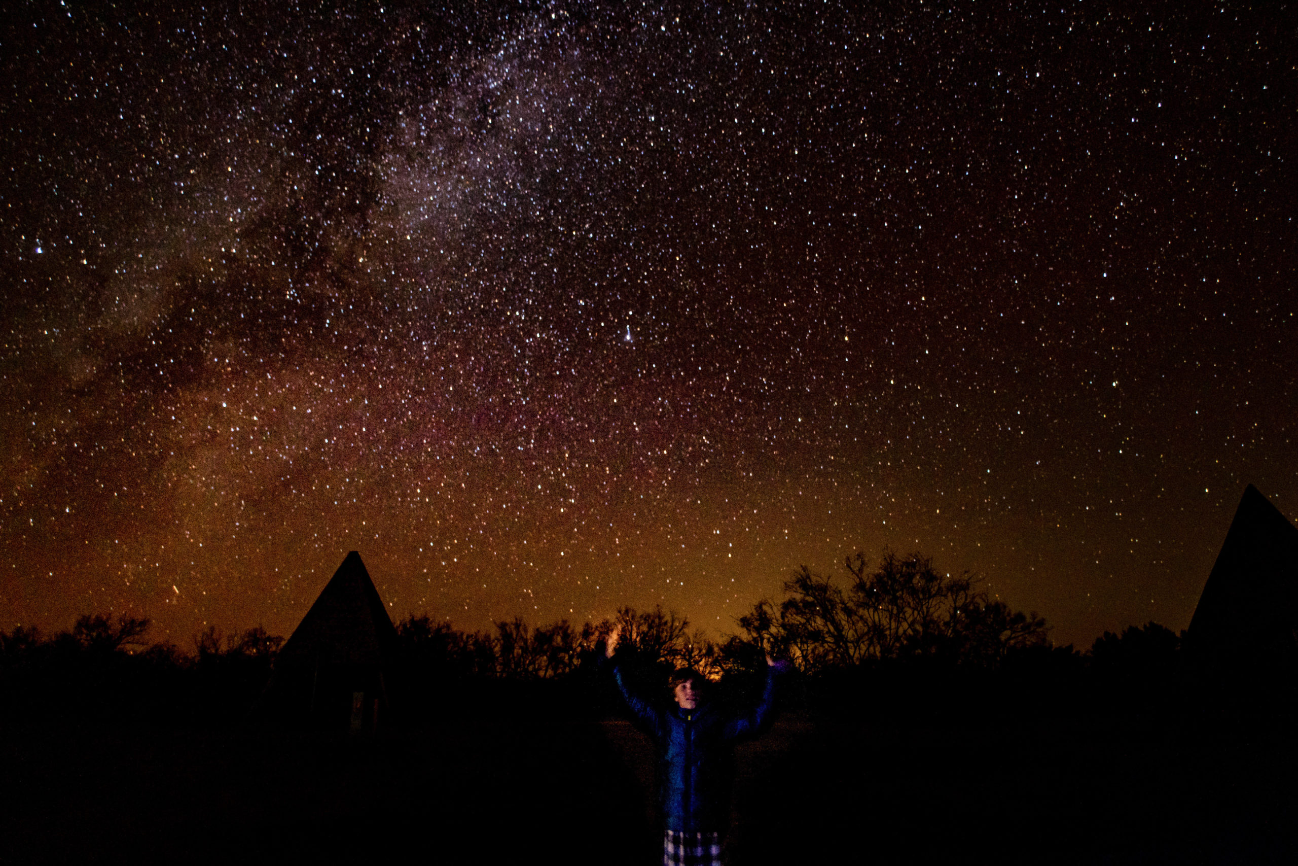 a boy stands in front of an orange night sky with thousands of stars