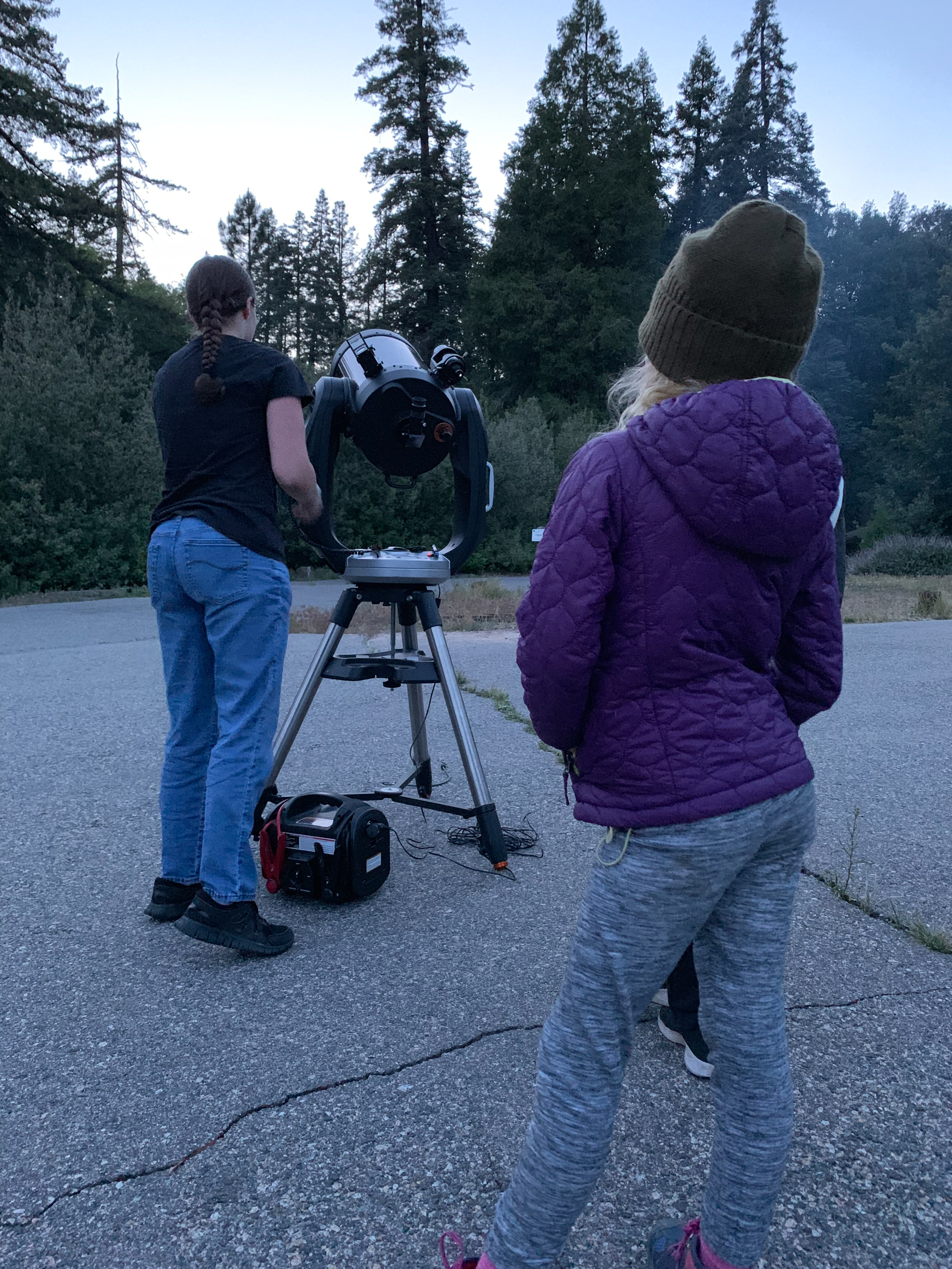 two people stand outside looking at a large telescope 