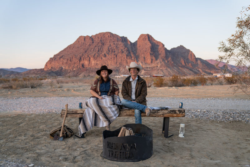 A man and woman sitting on a rustic bench at their RV campground in Texas