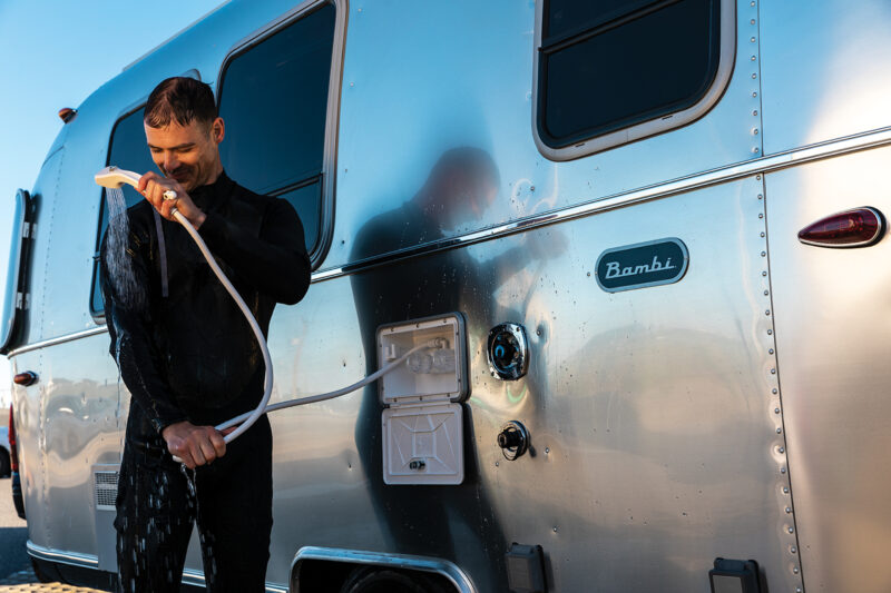 a man in a wet suit showers outside of an airstream bambi trailer