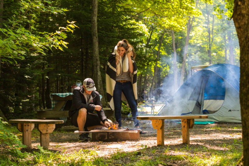 a couple stands over a campfire next to a tent in the woods
