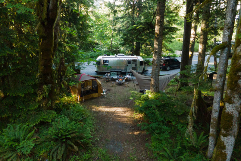a campsite with an airstream, tent and hammock in the woods