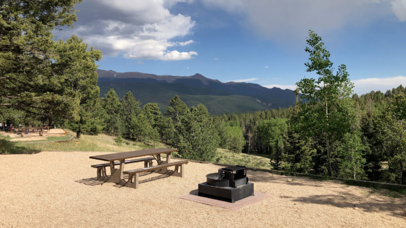 a picnic table and firepit at a campsite overlooking a scenic valley of greenery