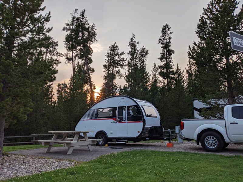a truck tows a small teardrop trailer and is parked at a campsite