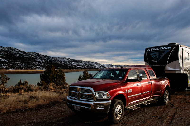 a red pickup truck tows an rv in front of a lake and snowy hills