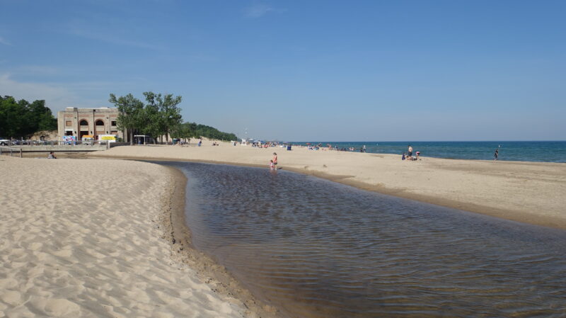 Wide sandy beach with beach house structure in the background. Families in the distance.