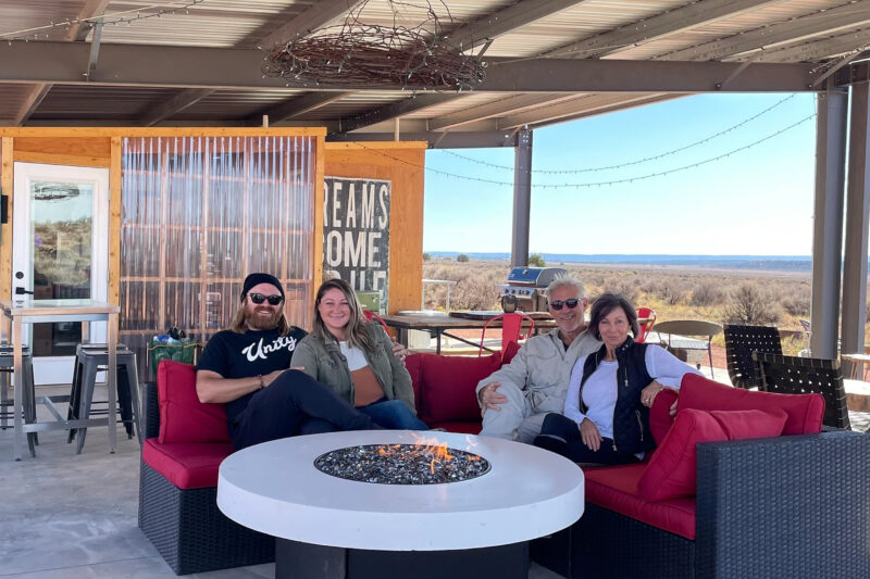 four people sit on a red couch around a fire pit