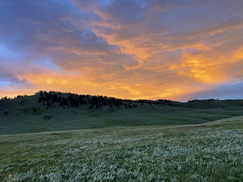 a large green field with a hill at sunset under orange and blue skies