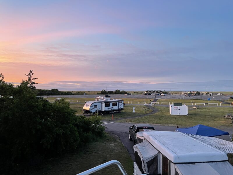 a campground with several RVs parked under a pink and purple sunset sky