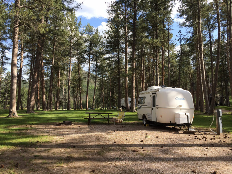 a small trailer is parked at a wooded campsite with a picnic table