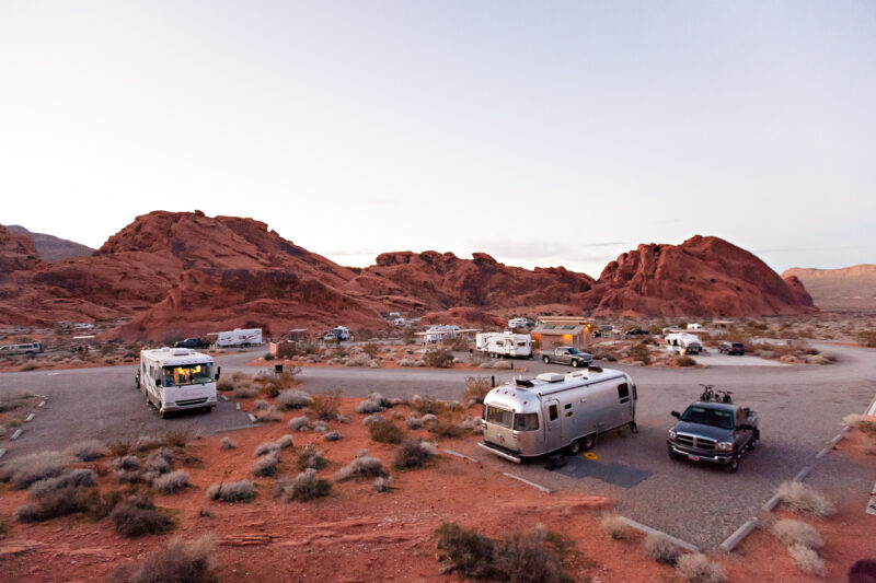 A group of RVs are stationed throughout a spacious campground surrounded by natural rock formations.