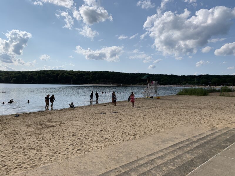 People stand on a sandy beach looking out at the water.