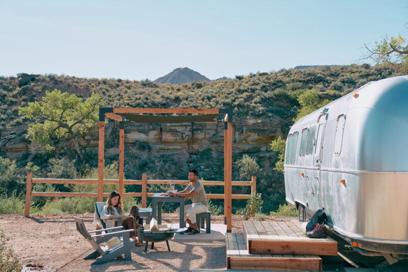 A family enjoys time together beneath a pergola next to their Airstream trailer