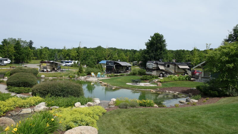 Large RV park with a pond, lush scenery, and several rigs parked at campsites