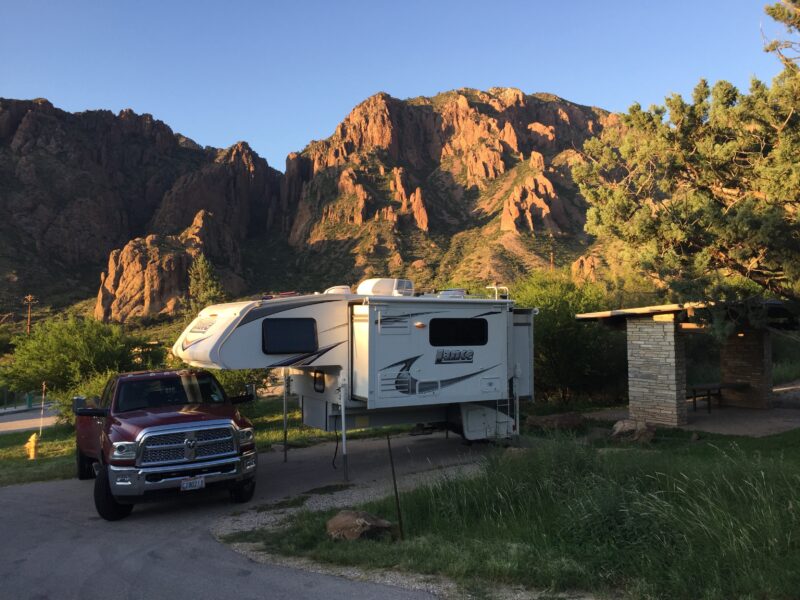A large truck camper sits at a campsite alongside a rocky landscape