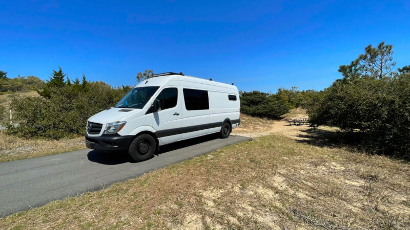 Campervan parked at a paved campsite in a sandy area
